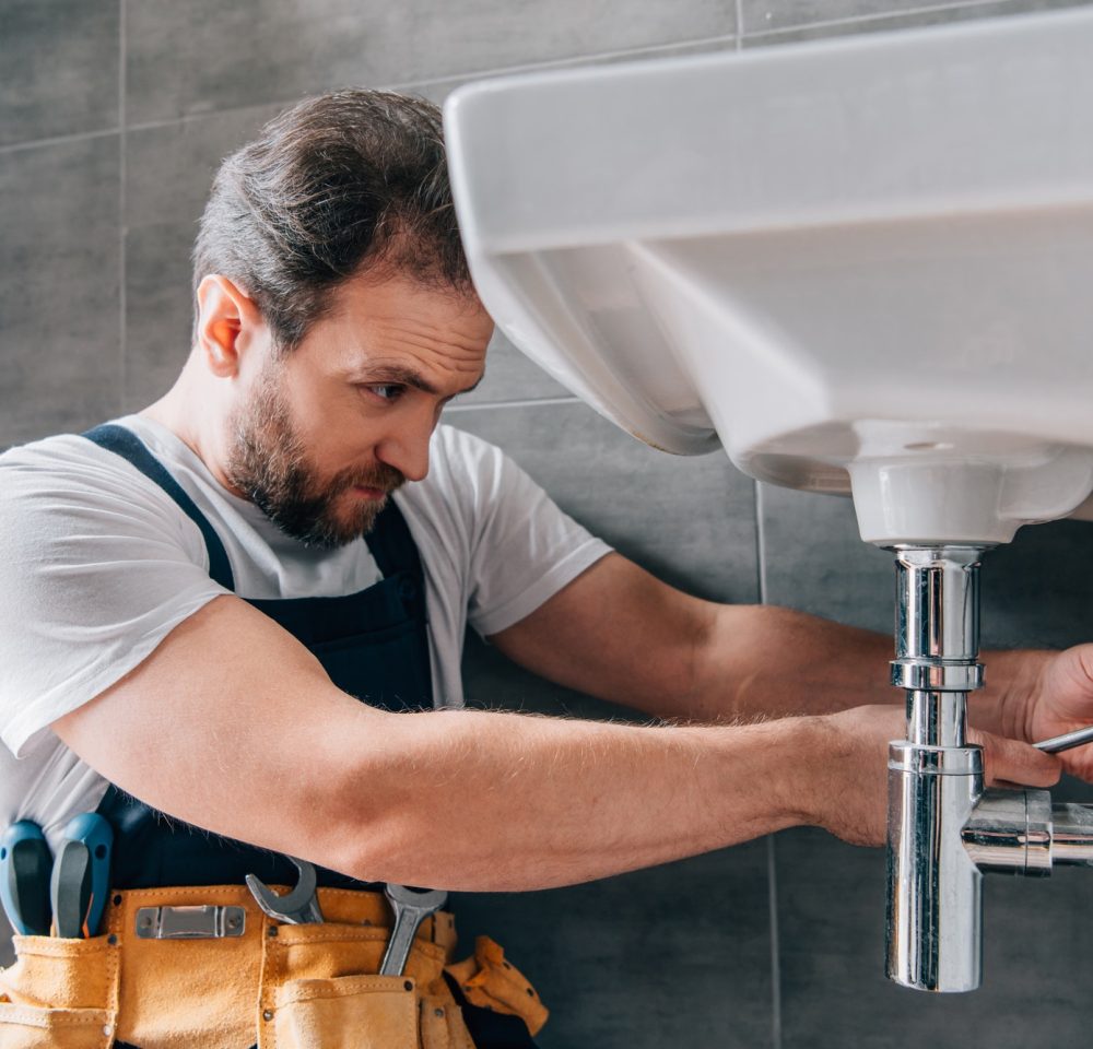 focused-male-plumber-in-working-overall-fixing-sink-in-bathroom.jpg